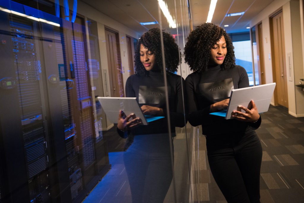 An African-American woman on a laptop in an office hallway.